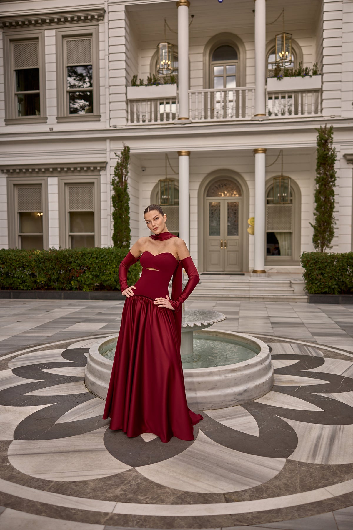 Model wearing Fiorence strapless satin evening gown with matching gloves and scarf detail in front of a luxury mansion