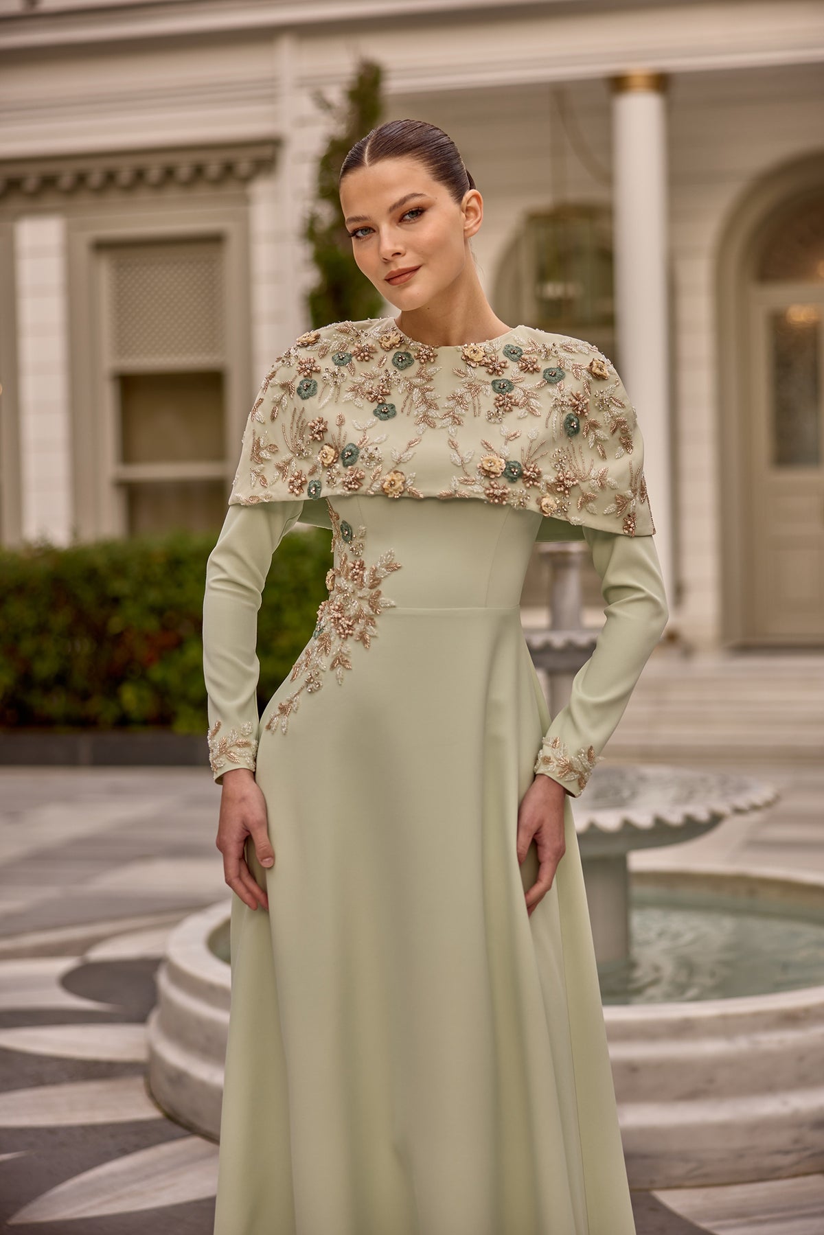 Model wearing Norah embellished long sleeve modest evening gown with floral cape detail