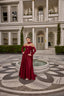 Model wearing Fiorence strapless satin evening gown with matching gloves and scarf detail in front of a luxury mansion