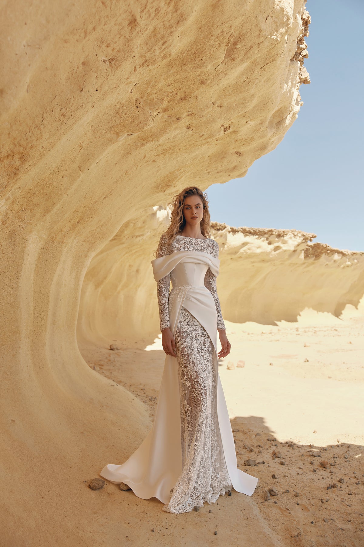 Yuma lace bridal gown with off-shoulder draped overlay and long sleeves in desert wedding setting